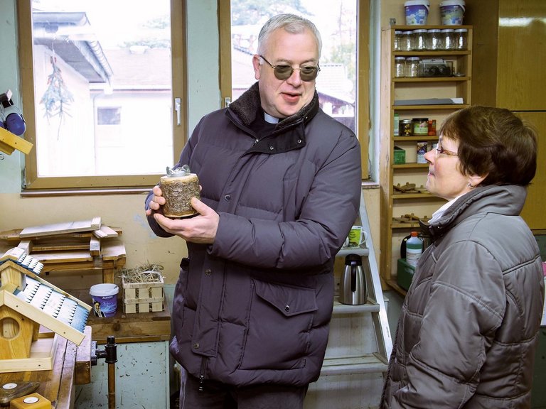 in der Werkstatt - ein Pater hält ein Werkstück in der Hand und spricht dabei mit einer Frau